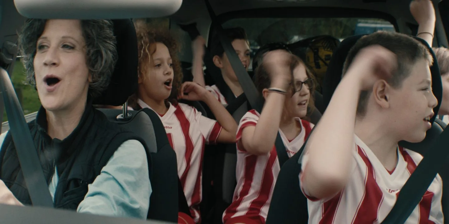 Children in football shirts singing along in a car