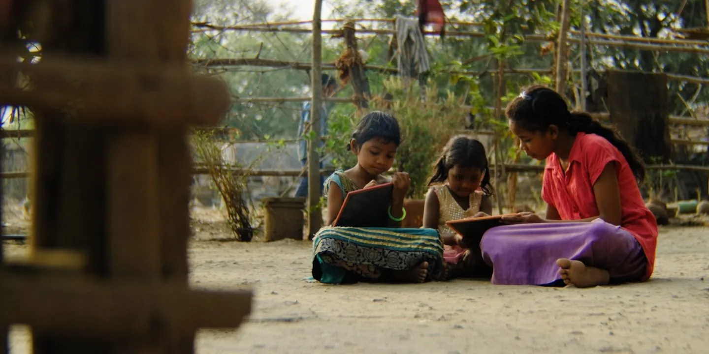 Three girls reading together outside a home in a rural village
