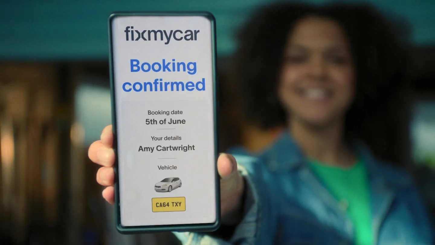 A customer holding up a phone showing a FixMyCar booking confirmation